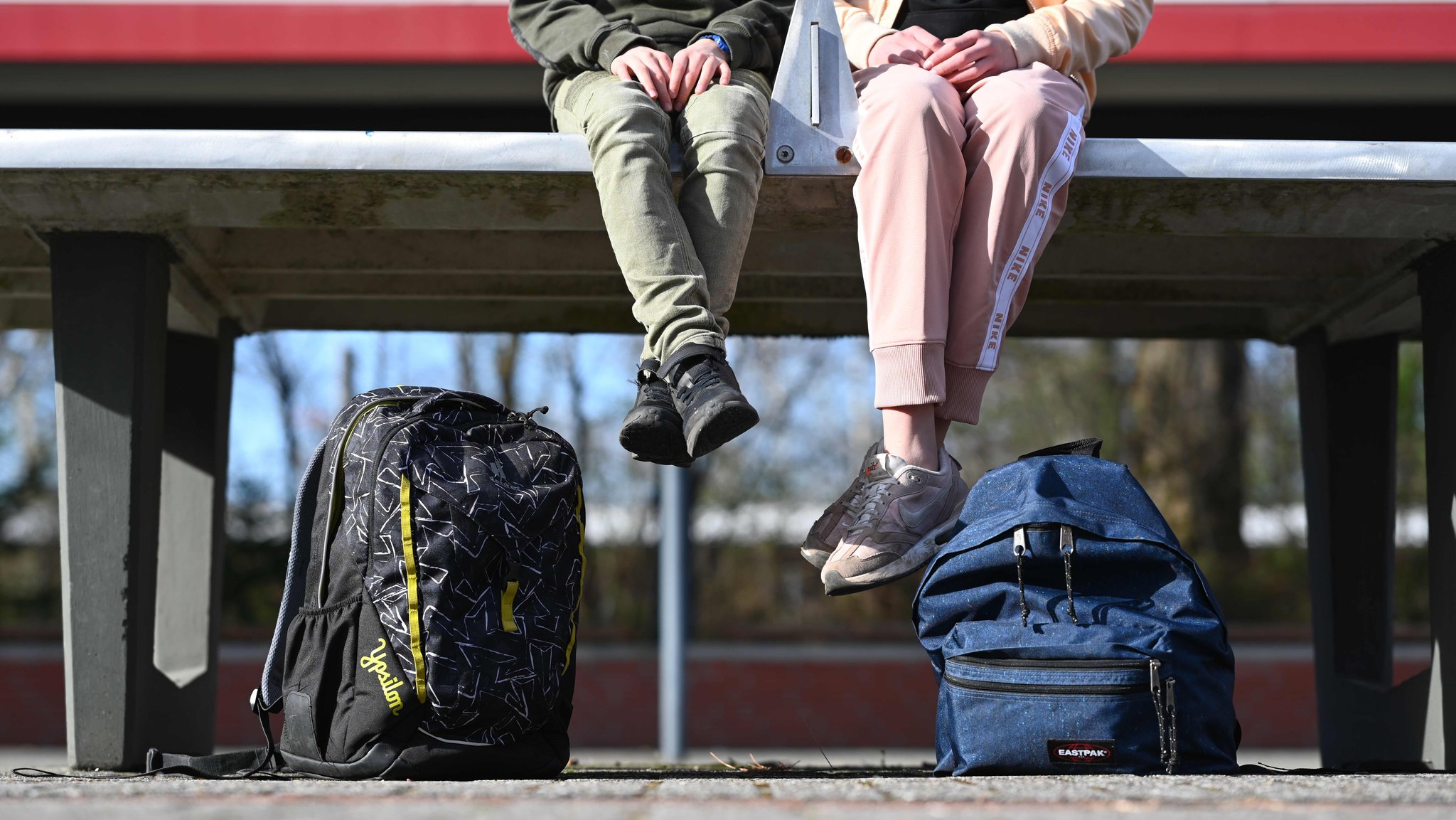 Schülerin und Schüler in Jogginghosen sitzen auf einem (Tischtennis-)Tisch auf dem Schulhof einer Schule.