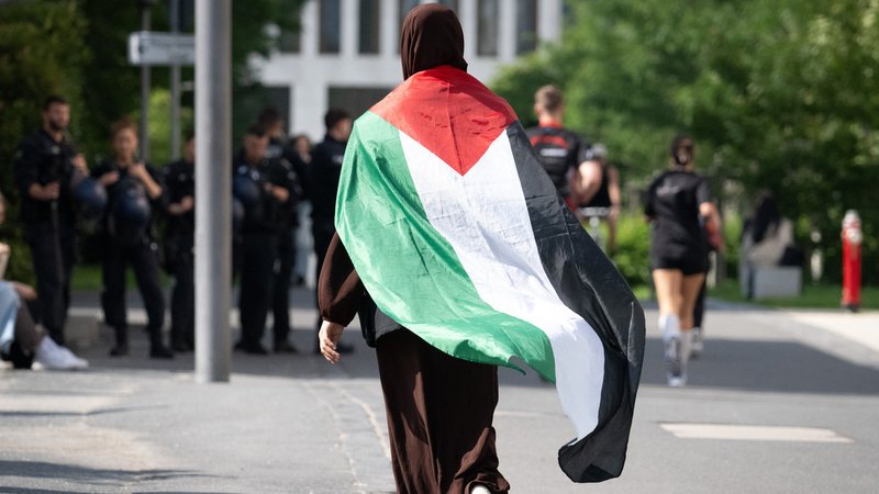 Eine Frau geht in Frankfurt am Main mit einer umgehängten Palästina-Fahne zu einer Demonstration (Archivbild)