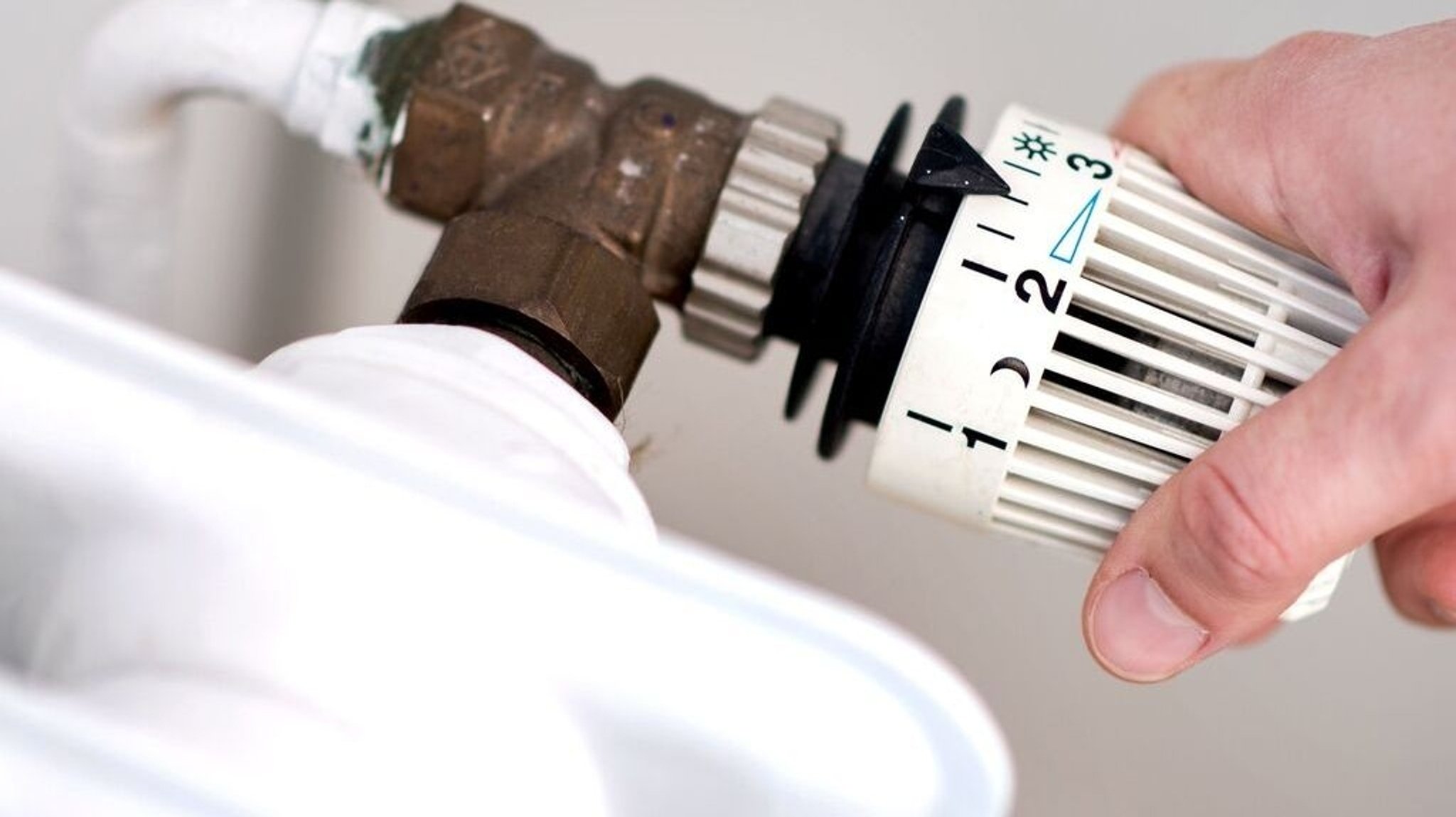 Jemand dreht am Thermostat eines Heizkörpers. 