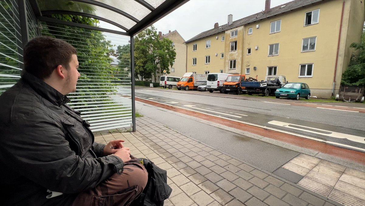 Ein Mann sitzt an einer Bushaltestelle.