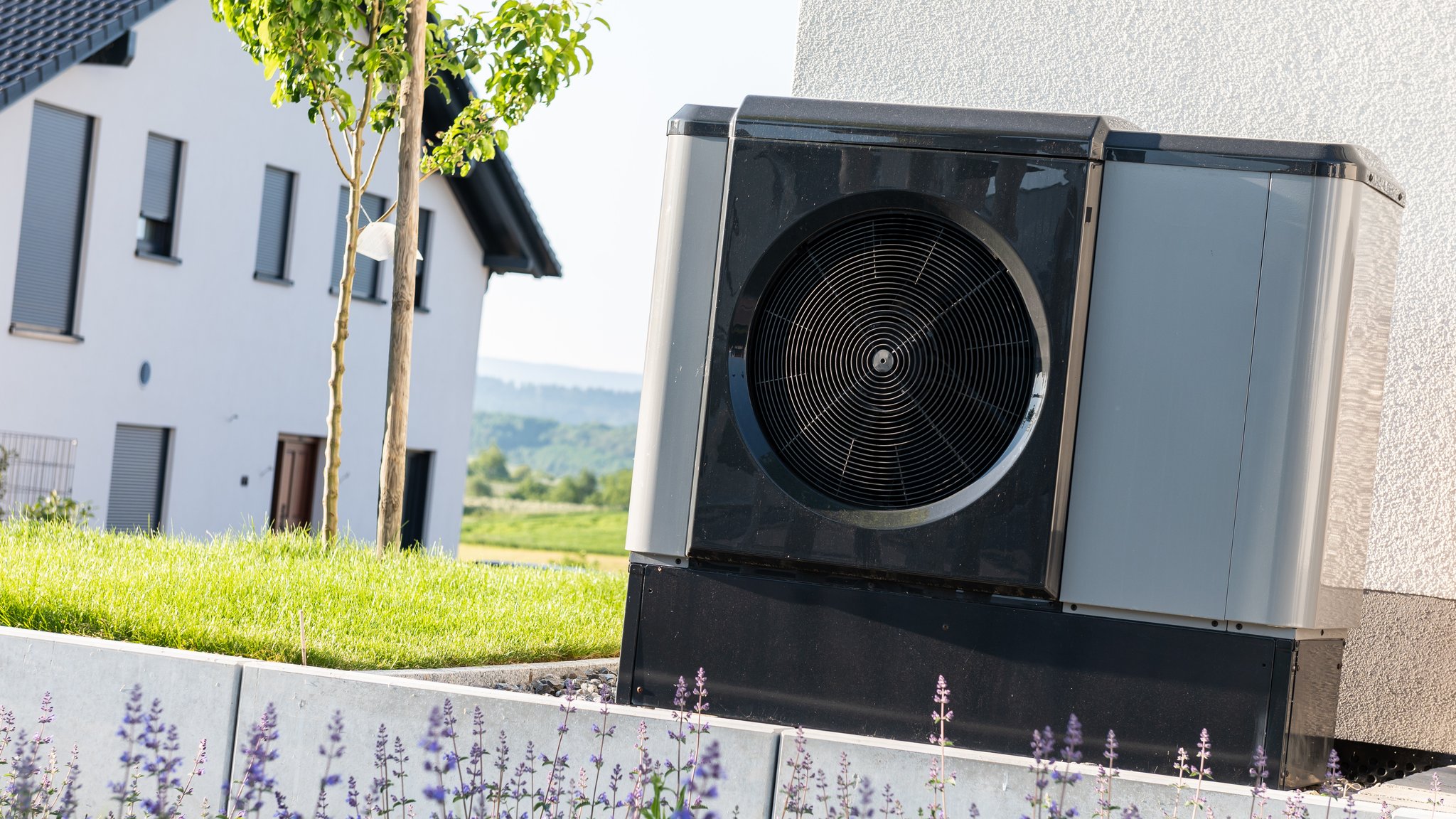 Eine Wärmepumpe steht in einem Garten eines Einfamilienhauses in einem Neubaugebiet.