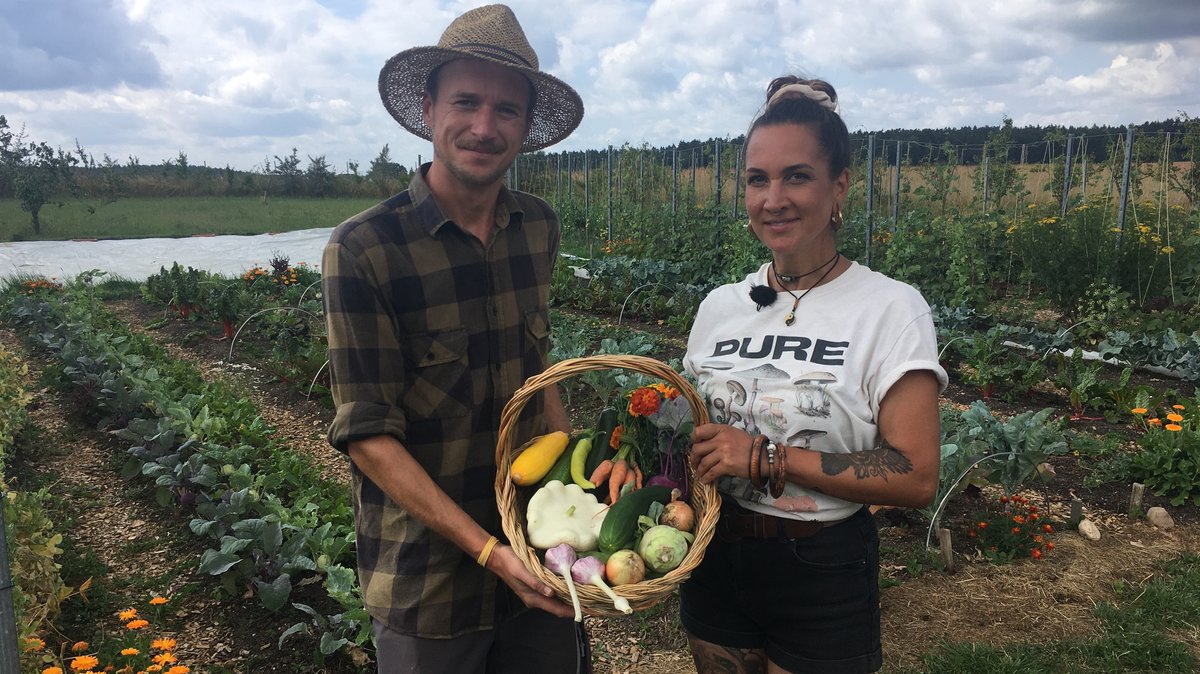 Ein Mann und eine Frau stehen in einem Garten und halten einen Korb mit Gemüse.