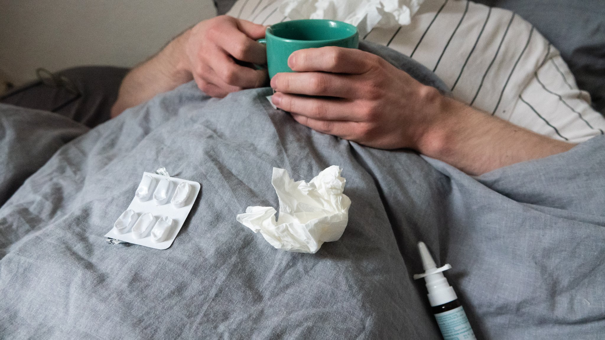 Mann im Bett mit Teetasse, Tabletten und Taschentüchern