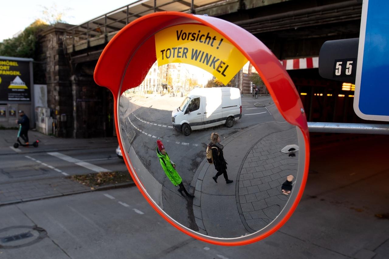 Ein Trixi-Spiegel mit dem Hinweis "Vorsicht! Toter Winkel" hängt an einer Straßenkreuzung in München. Der Spiegel soll den toten Winkel beim Abbiegen von großen Fahrzeugen reduzieren und damit die Sicht auf Fußgänger und Radfahrer verbessern. 