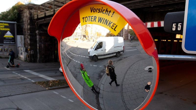 Ein Trixi-Spiegel mit dem Hinweis "Vorsicht! Toter Winkel" hängt an einer Straßenkreuzung in München. Der Spiegel soll den toten Winkel beim Abbiegen von großen Fahrzeugen reduzieren und damit die Sicht auf Fußgänger und Radfahrer verbessern. 