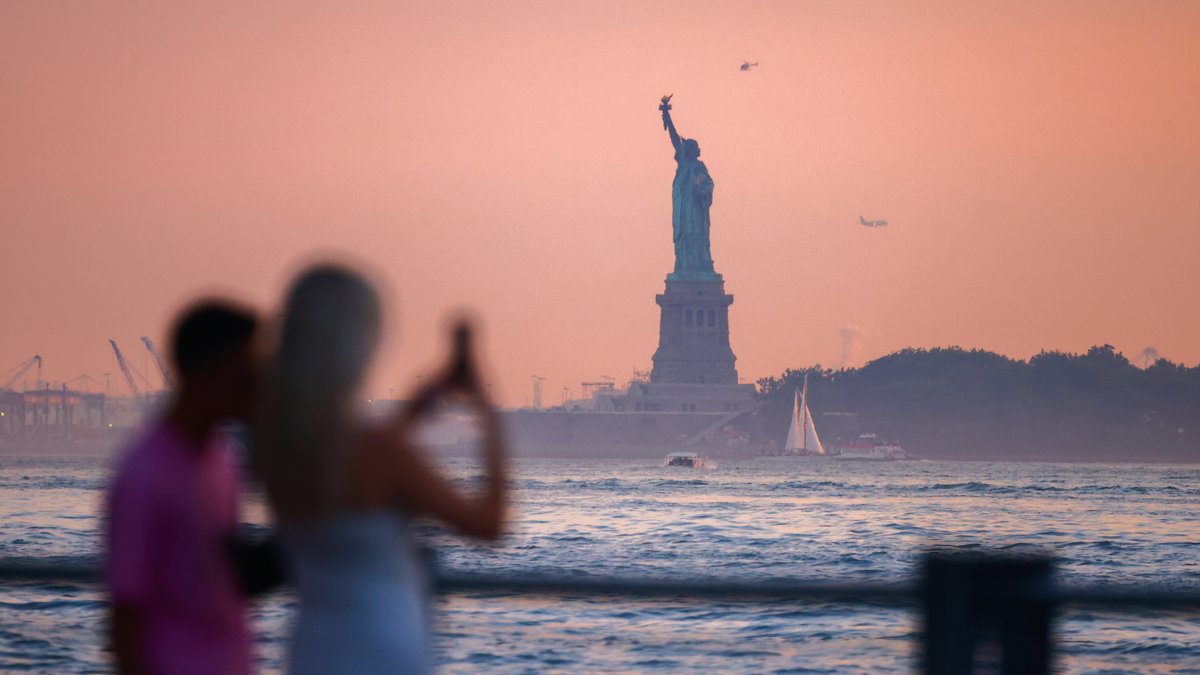Touristen fotografieren die Freiheitsstatue in den USA in der Dämmerung | Bild: picture alliance / NurPhoto | Beata Zawrzel Touristen fotografieren die Freiheitsstatue in den USA in der Dämmerung
