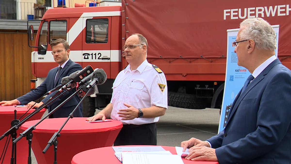 Vor einem Feuerwehrauto stehen zwei Männer und Innenminister Joachim Herrmann und sprechen in Mikrofone.