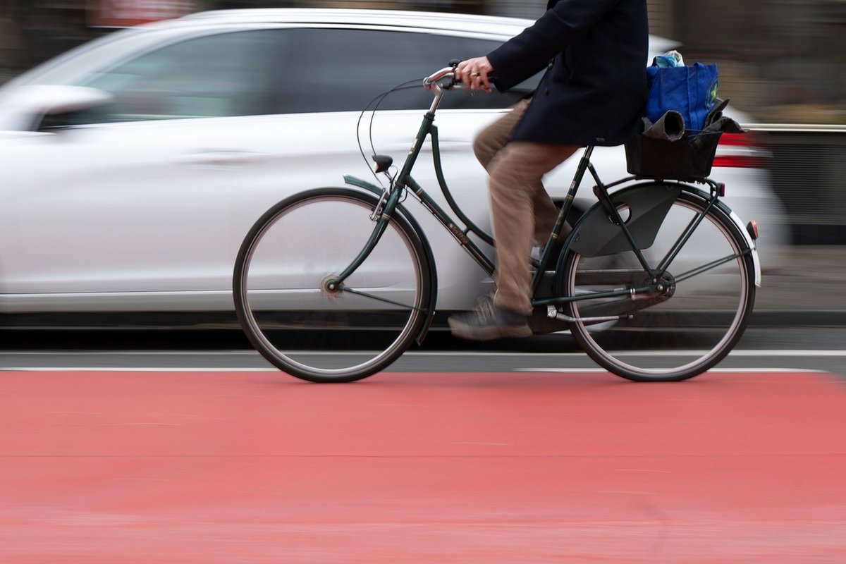 Ein Fahrradfahrer fährt auf einer Fahrradstraße an einem Schutzstreifen für geöffnete Türen an Autos vorbei. Der Schutzstreifen soll verhindern, dass Fahrradfahrer durch unachtsam geöffnete Türen verletzt werden. 