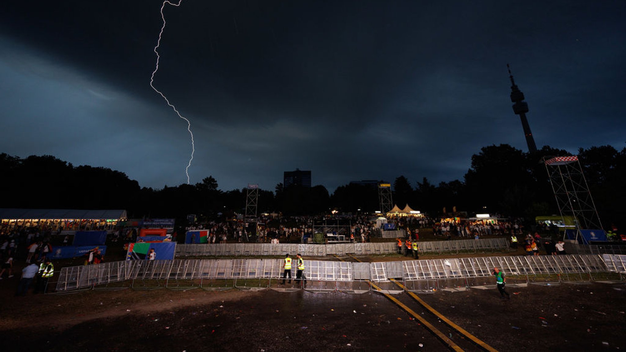 dpatopbilder - 29.06.2024, Nordrhein-Westfalen, Dortmund: Fußball, UEFA Euro 2024, EM, Deutschland - Dänemark, Finalrunde, Achtelfinale, Für die Fans der deutschen Fußball-Nationalmannschaft, die beim Fanfest in der Fanzone vor einer Leinwand stehen, ist die TV-Übertragung wegen eines Unwetters beendet worden. Ein Blitz ist am dunklen Himmel zu sehen. Foto: Friso Gentsch/dpa +++ dpa-Bildfunk +++