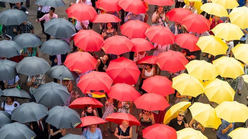 Menschen mit schwarz-rot-goldenen Regenschirmen nach ihrem Einbürgerungsfest vor dem sächsischen Landtag in Dresden