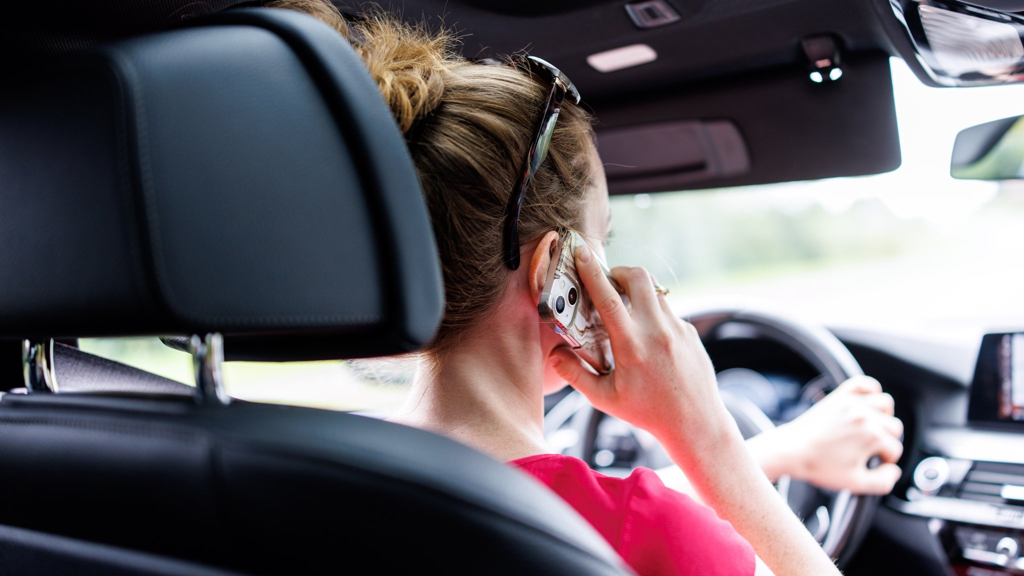 Ein Frau telefoniert beim Autofahren mit ihrem Handy am Ohr.